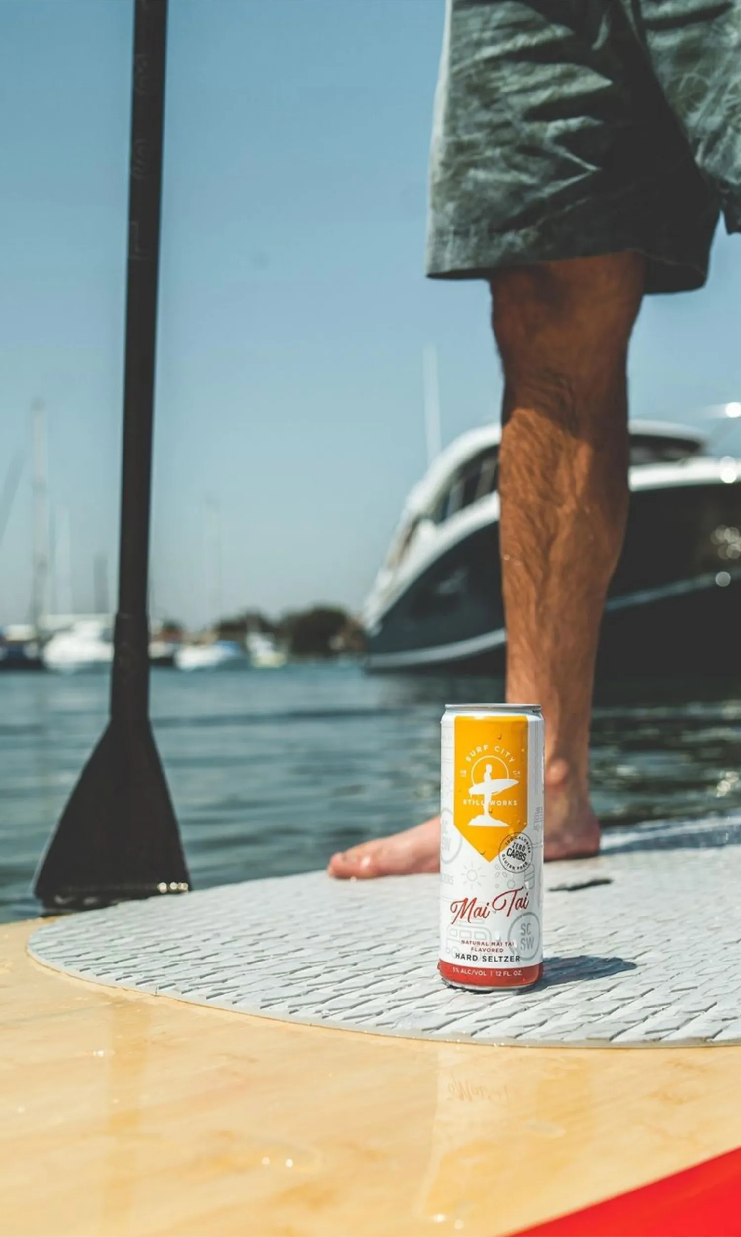 Person on a paddleboard beside a can of Surf City hard seltzer.