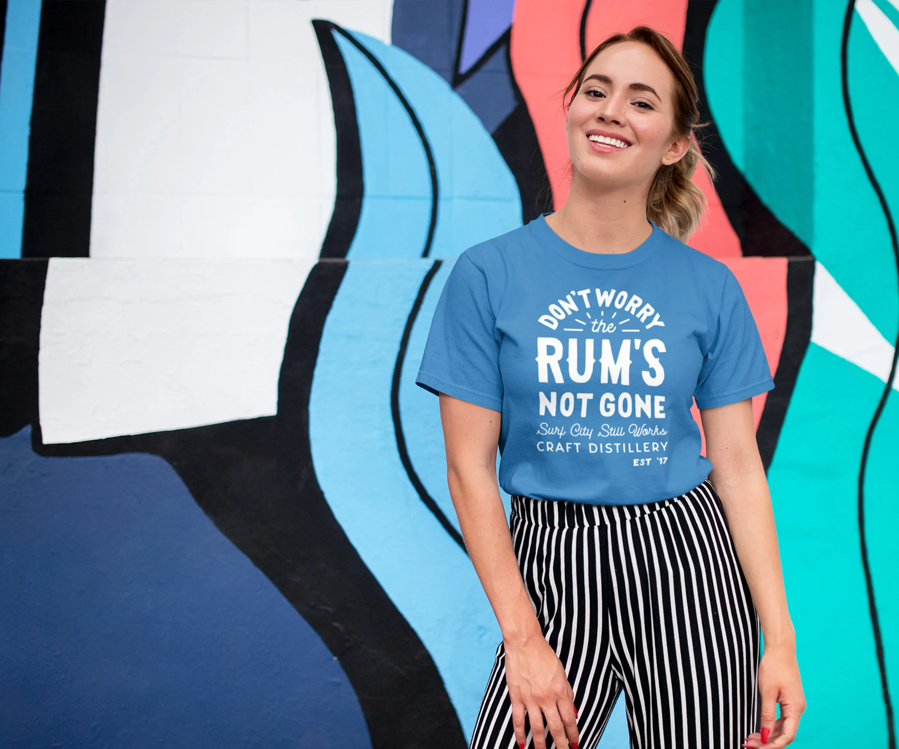 Woman in a "Don’t worry, the rum’s not gone" tee against a surf mural.