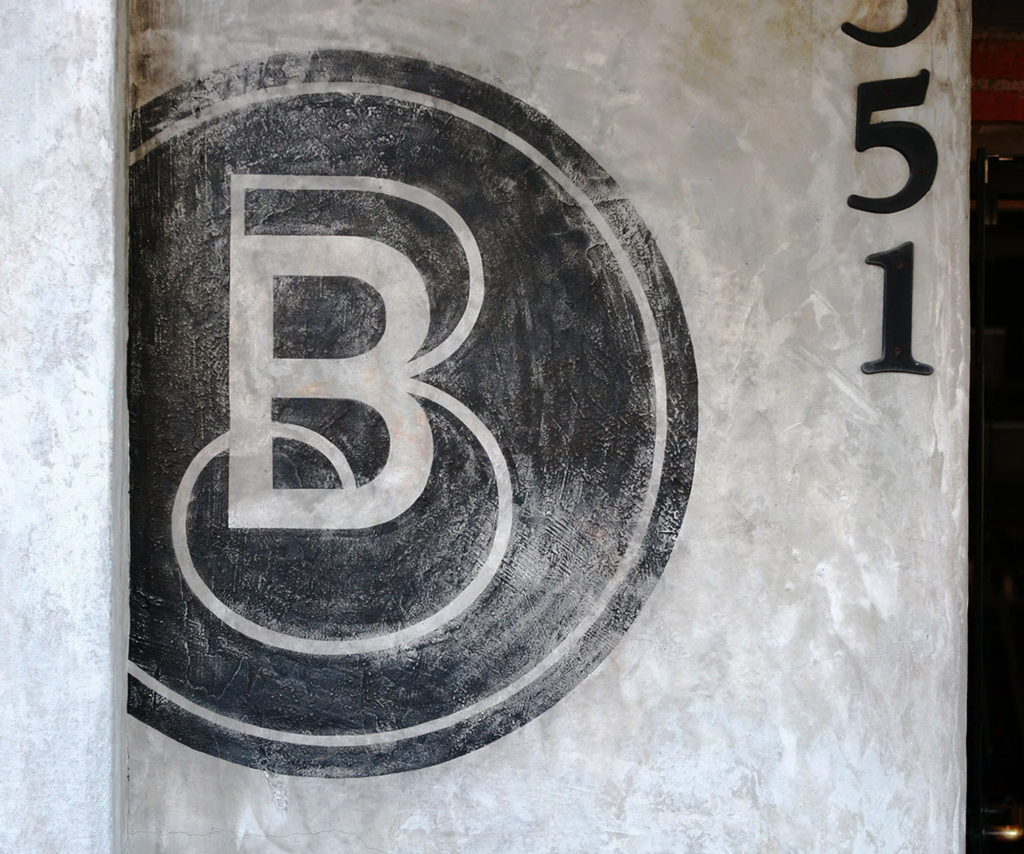 Blue Butterfly monogram painted on a concrete wall beside a street number.