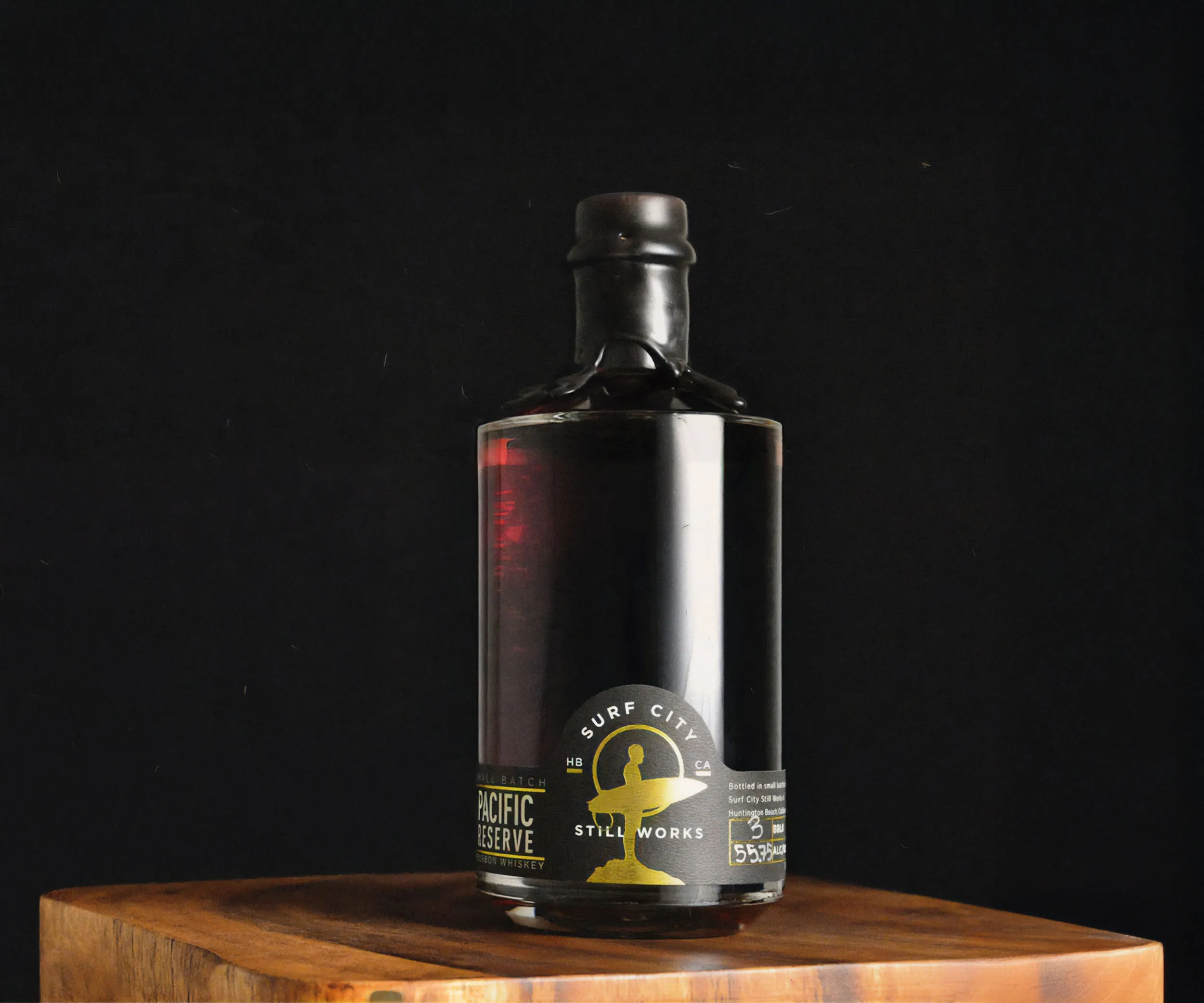 Dark spirit bottle lit dramatically on a wooden block.