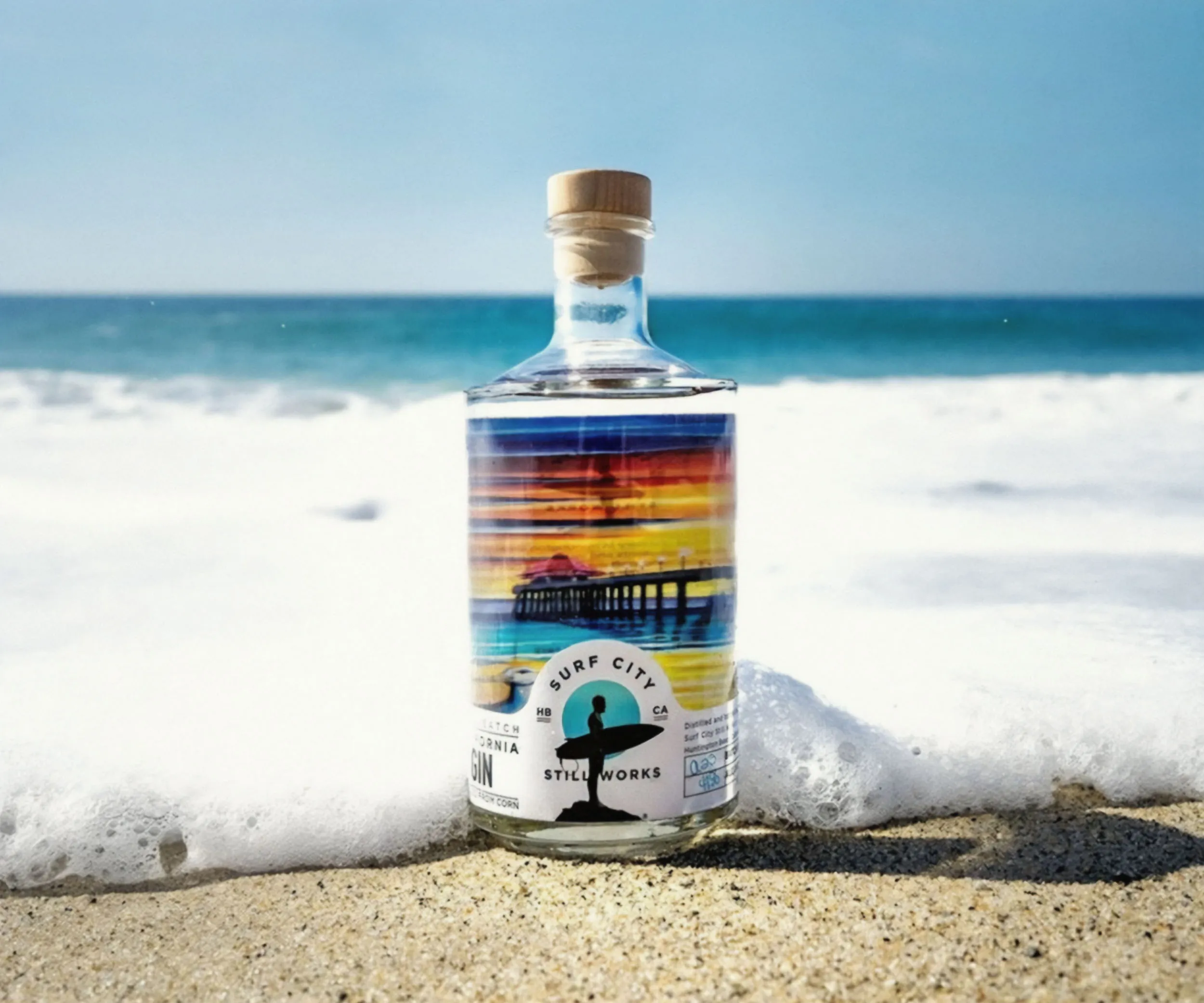 Bottle with a sunset-stripe label in the surf at the water’s edge.