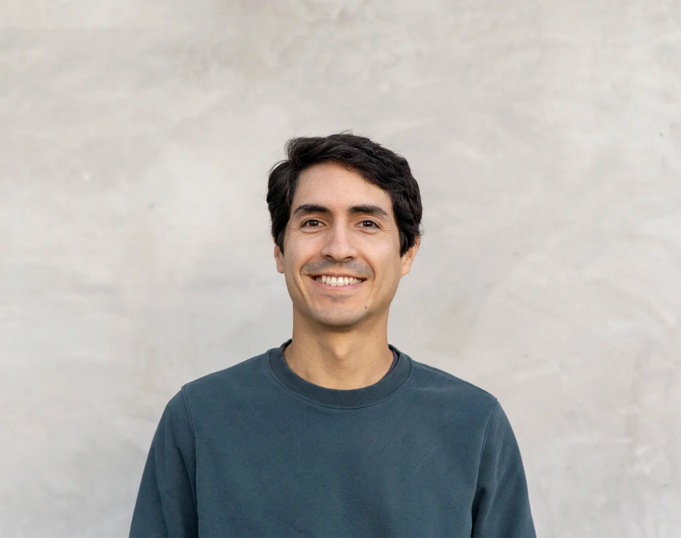 Edgar Tsuge, smiling, in front of a plaster wall.